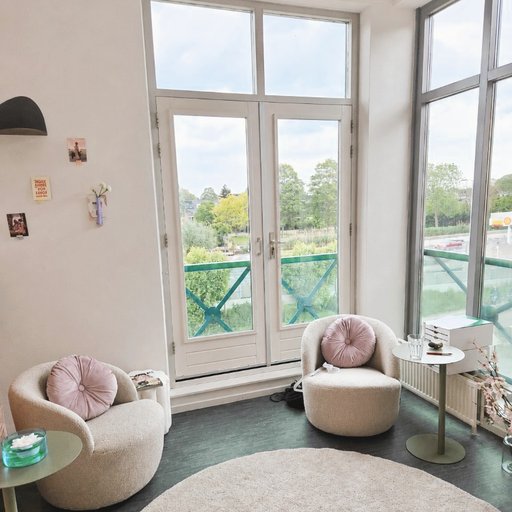 Twee fauteuils in een lichte praktijkruimte met groot raam en uitzicht op groen